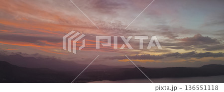 Dramatic evening sky over Crete island with colorful sunset clouds, silhouetted mountains, coastal village lights, and calm dark sea under twilight 136551118