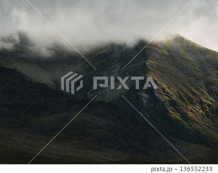 Misty mountains shrouded in atmospheric haze. Sunlight highlights a stark mountain ridge. Misty mountains shrouded in atmospheric haze. Sunlight highlights a stark mountain ridge. 136552233