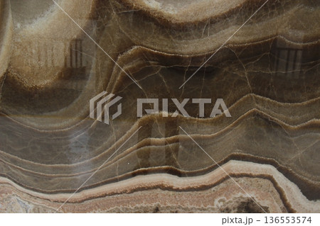Close up of brown onyx marble stone texture showing natural sedimentary wave patterns and dense mineral crystals. Close up of brown onyx marble stone texture showing natural sedimentary wave patterns and dense mineral crystals. 136553574