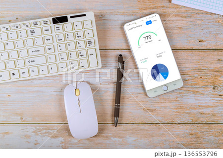 Device displays credit summary with keyboard, mouse on wooden table in home office setting 136553796