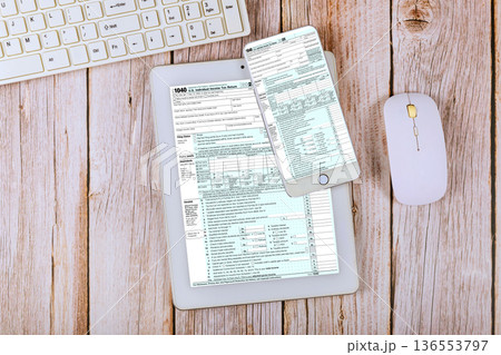 Tax forms displayed on PC tablet smartphone next to computer keyboard mouse in accounting office Tax forms displayed on PC tablet smartphone next to computer keyboard mouse in accounting office 136553797