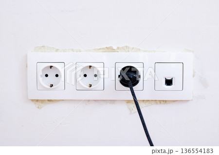 Outdated wall socket featuring black plug and network port on stained plaster surface 136554183