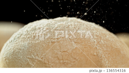 Static shot of a leavened dough loaf isolated on black background with falling flour. Concept of baking, artisan bread making and dough preparation. 136554316
