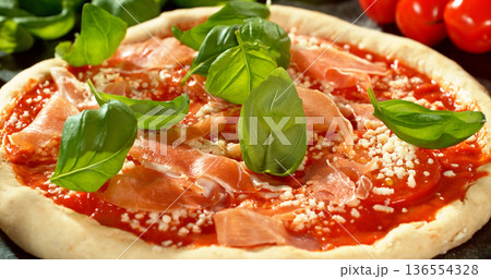 Shot of fresh basil leaves falling onto raw pizza dough topped with tomato sauce and mozzarella. Cinematic detail of Italian pizza preparation on a floured wooden table. Shot of fresh basil leaves falling onto raw pizza dough topped with tomato sauce and mozzarella. Cinematic detail of Italian pizza preparation on a floured wooden table. 136554328