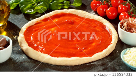 Prepared pizza dough with tomato sauce and mozzarella. Italian pizza preparation on rustic wooden table. Prepared pizza dough with tomato sauce and mozzarella. Italian pizza preparation on rustic wooden table. 136554332