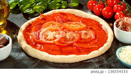 Fresh sliced tomatoes falling into rich tomato sauce on raw pizza dough. Cinematic food preparation shot capturing splash, texture and motion in detail. 136554333