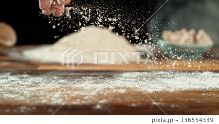 Close up of bakers hand tossing flour over prepared risen dough on wooden table. Cinematic baking concept, artisan bread preparation and texture detail. 136554339