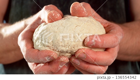 Closeup of a bakers hands kneading and stretching freshly risen dough. Detailed texture and elasticity visible in cinematic light. Concept of yeast dough preparation and traditional baking process. Closeup of a bakers hands kneading and stretching freshly risen dough. Detailed texture and elasticity visible in cinematic light. Concept of yeast dough preparation and traditional baking process. 136554342