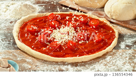 Closeup of grated mozzarella falling onto fresh pizza with tomato sauce and sliced tomatoes. Detailed texture, flying cheese particles and dynamic motion. Concept of pizza preparation and cooking. 136554346