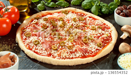 Prepared pizza dough with tomato sauce and mozzarella. Italian pizza preparation on rustic wooden table. 136554352