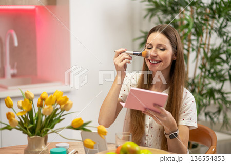 Smiling young long-haired woman doing make up and looking excited 136554853