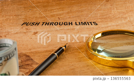 PUSH THROUGH LIMITS on wood with US dollars, elegant pen, and golden magnifier. Represents business strategy and growth 136555563