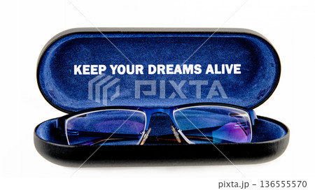 Blue framed glasses sit inside an open black case with a blue felt interior. The inspiring text KEEP YOUR DREAMS ALIVE is visible on the case lid 136555570