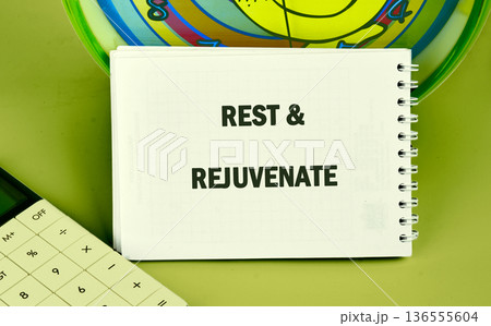 A note saying rest and rejuvenate is on a table next to a calculator and a colorful clock. The setting shows a workspace with a simple layout 136555604