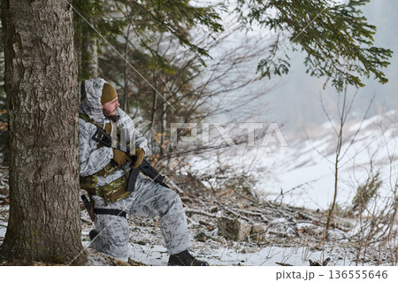 Soldier In Winter Camouflage Kneeling Against Tree With Rifle In Snowy Forest Patrol Soldier In Winter Camouflage Kneeling Against Tree With Rifle In Snowy Forest Patrol 136555646