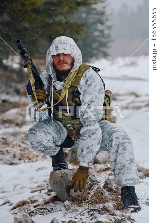 Armed Soldier In Winter Camouflage Crouching With Rifle And Tactical Gear In Snowy Forest 136555655