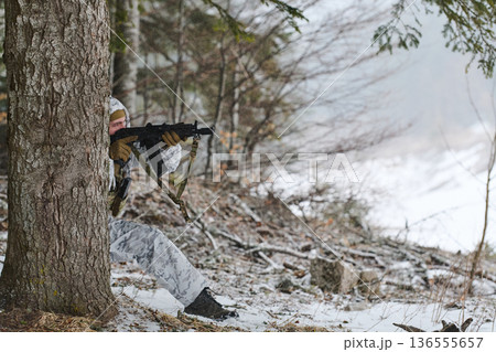 Soldier in Winter Camouflage Aiming Rifle Behind Tree in Snowy Forest During Training 136555657