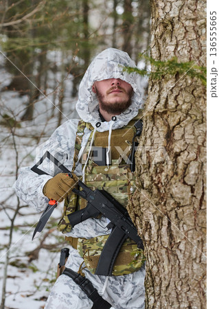 Soldier In Winter Camouflage With Rifle And Knife Hiding Behind Tree In Snowy Forest Soldier In Winter Camouflage With Rifle And Knife Hiding Behind Tree In Snowy Forest 136555665