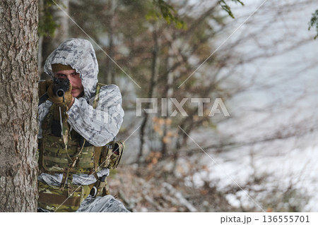 Soldier In Winter Camouflage Taking Aim Behind Tree During Cold Weather Training Exercise 136555701