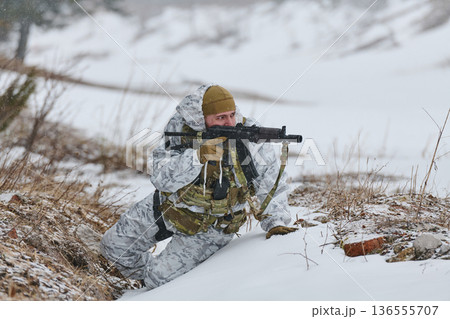 Soldier In Winter Camouflage With Rifle Crawling Through Snowy Field During Military Training Exercise Soldier In Winter Camouflage With Rifle Crawling Through Snowy Field During Military Training Exercise 136555707