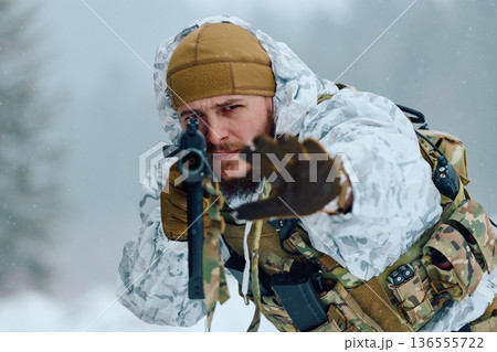 Winter Soldier In Snow Camouflage Aiming Rifle While Advancing Through Forested Snowfield 136555722