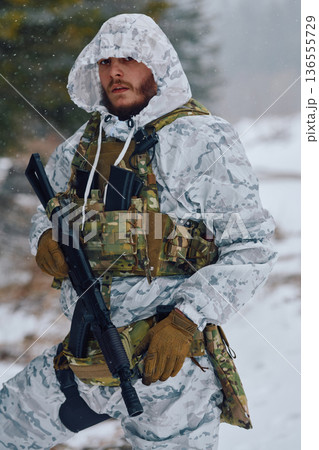 Armed Soldier in Winter Camouflage With Tactical Vest and Rifle Standing in Snowy Forest Armed Soldier in Winter Camouflage With Tactical Vest and Rifle Standing in Snowy Forest 136555729