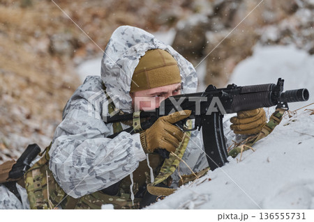 Soldier in Winter Camouflage Aiming Rifle While Lying in Snow During Military Training Exercise Soldier in Winter Camouflage Aiming Rifle While Lying in Snow During Military Training Exercise 136555731