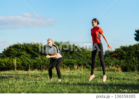 Two women exercise on a grassy field in daylight 136556305