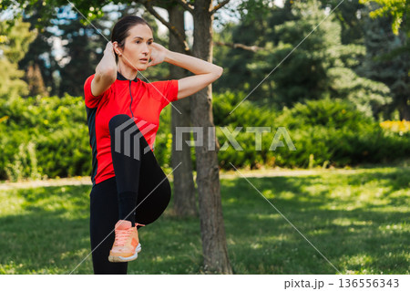 Woman exercises in park during sunny day 136556343