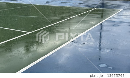 Wet tennis court surface reflecting soft clouds, ideal for sports-themed background or banner Wet tennis court surface reflecting soft clouds, ideal for sports-themed background or banner 136557454
