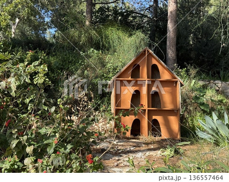 Orange wooden birdhouse in lush garden surrounded by greenery and vibrant flowers 136557464