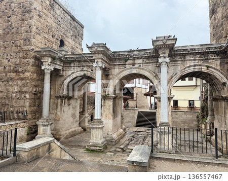 Ancient Roman triumphal arch with three arches and historical stone architecture in overcast weather Ancient Roman triumphal arch with three arches and historical stone architecture in overcast weather 136557467