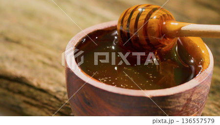 Honey dripping from a wooden stick into a bowl on a wooden surface at a local market in the afternoon 136557579