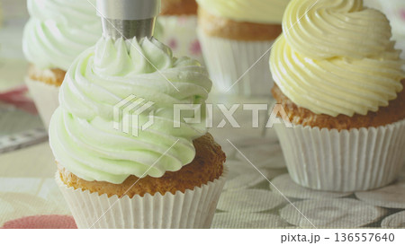 Bakers decorate cupcakes with green and yellow frosting in a kitchen during the afternoon 136557640