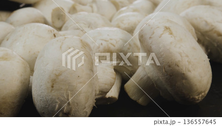 Fresh white mushrooms are gathered on a surface and ready for cooking or preparation in a kitchen setting 136557645