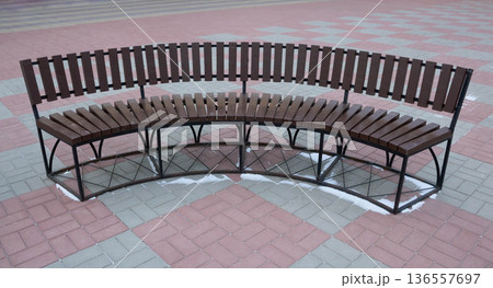 A brown semi-circular bench in a park square. 136557697