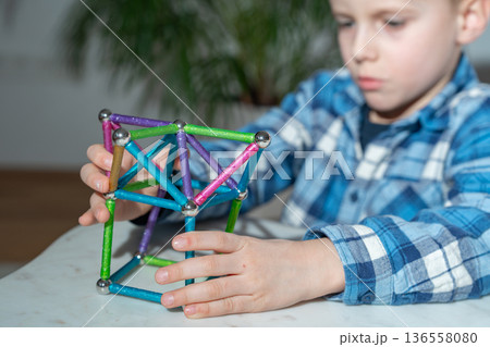 Young boy focused on assembling a colorful magnetic construction set at the table. Indoor activity scene. Concept of concentration, early education, creativity and logical thinking development Young boy focused on assembling a colorful magnetic construction set at the table. Indoor activity scene. Concept of concentration, early education, creativity and logical thinking development 136558080