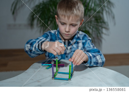Child engaged in hands-on learning activity at home using a colorful magnetic construction set. Homeschooling concept, cognitive growth, creative exploration and screen-free educational play 136558081
