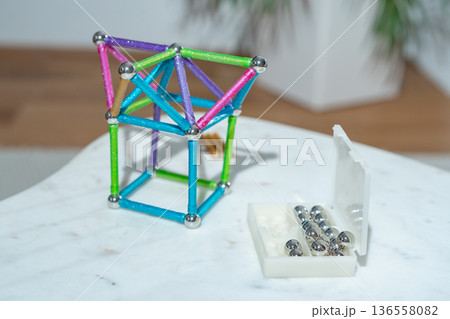 Magnetic building structure made of bright rods and steel spheres on a white table. Indoor lifestyle scene. Concept of early education, imagination, engineering thinking and child development. 136558082