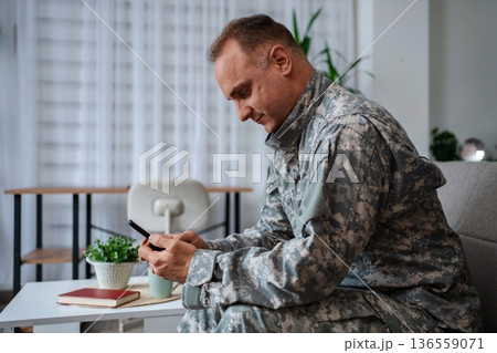 Soldier in camouflage uniform using smartphone at home 136559071