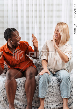 Two excited female friends cheering and high-fiving on the sofa 136559133
