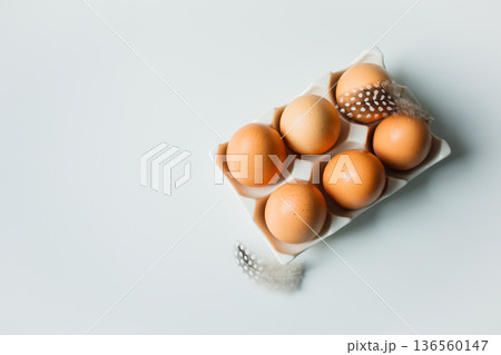 Chicken eggs on a stand with chicken feathers: minimalistic Easter flat lay on white background. Easter food, preparation for Easter holidays 136560147