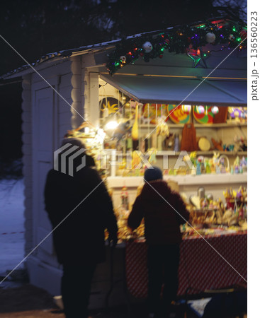 Christmas market with illuminated food stalls, gift shops and kiosks, New Year outdoor fair decorations, garlands and festoons, Xmas atmosphere, retail and store illumination, decor in Europe city Christmas market with illuminated food stalls, gift shops and kiosks, New Year outdoor fair decorations, garlands and festoons, Xmas atmosphere, retail and store illumination, decor in Europe city 136560223