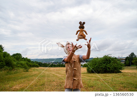 Girl in bunny costume and hat with long ears, playing with stuffed toy in field under cloudy sky 136560530