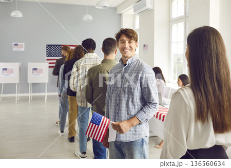 Happy young male American voter with flag of USA standing in line at polling station Happy young male American voter with flag of USA standing in line at polling station 136560634