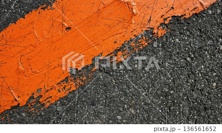 Macro view of vibrant orange paint stroke texture on rough black asphalt road surface background Macro view of vibrant orange paint stroke texture on rough black asphalt road surface background 136561652