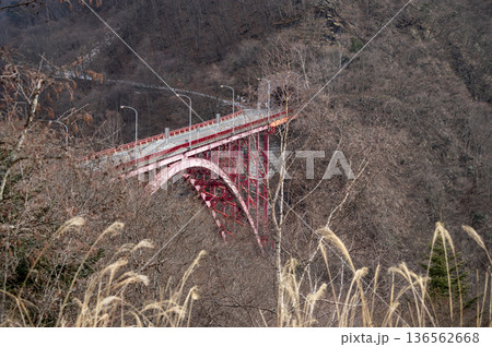 冬の奥秩父の彩甲斐街道に架かる赤いアーチ橋「豆焼橋」と山々の風景 136562668