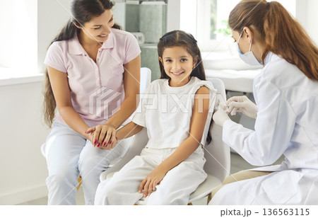 Doctor administering vaccine to school-age girl as supportive mother holds her hand Doctor administering vaccine to school-age girl as supportive mother holds her hand 136563115