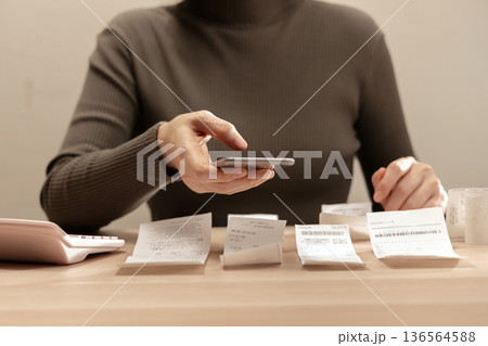 Women using smartphone calculate paper receipts on table. Calculating bills, expense tracking, personal finance 136564588