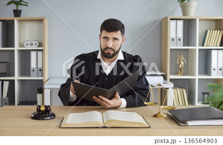 Judge signing case documents at desk with gavel, open law book and scales Judge signing case documents at desk with gavel, open law book and scales 136564903